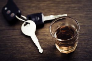 A glass of whisky and a set of car keys on a wooden table